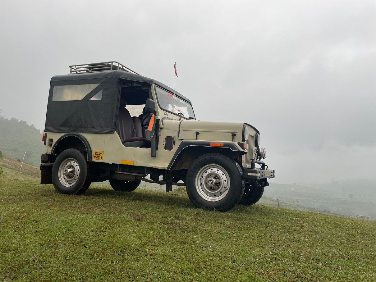 A jeep parked on a grassy field with a cloudy sky